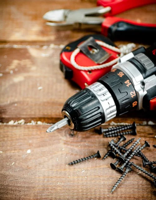 Cordless drill, tape measure and screws on a workbench